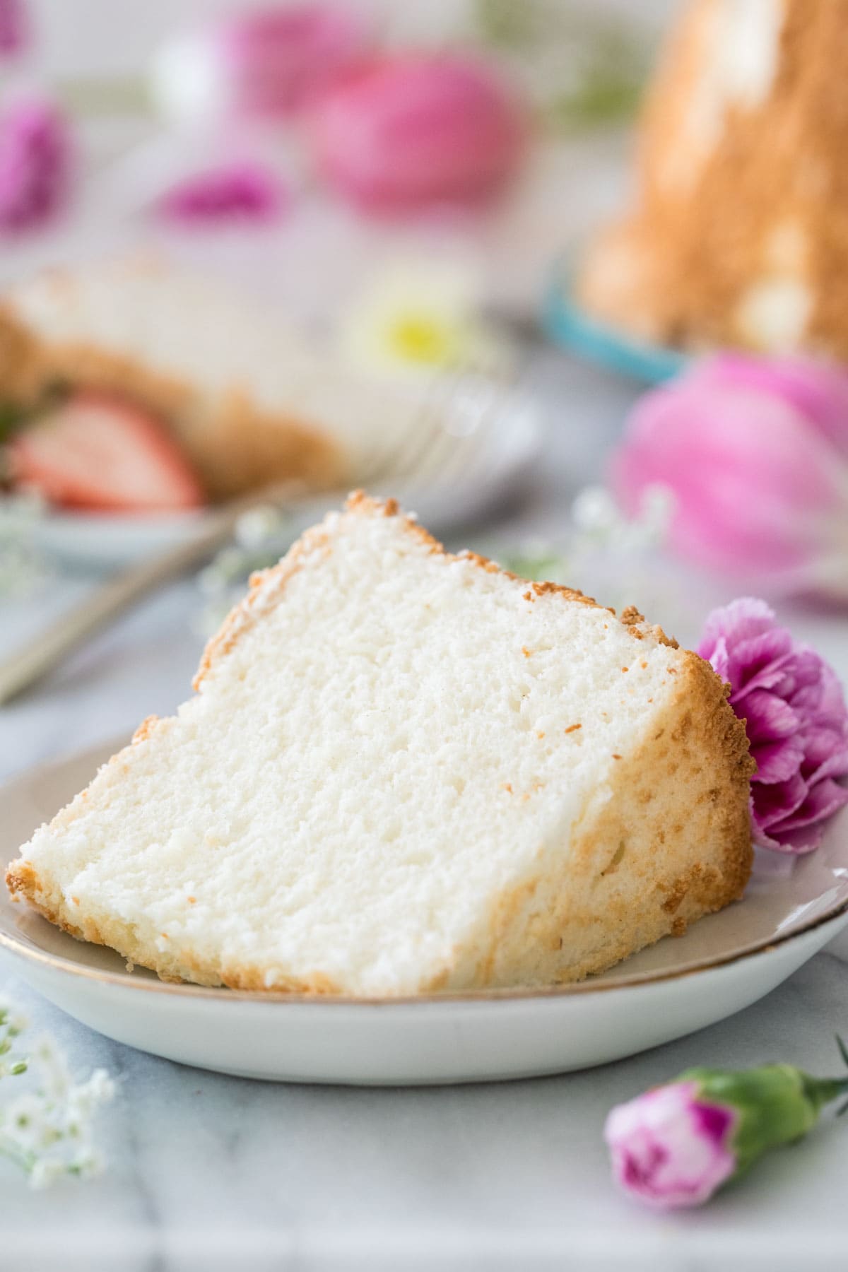 Angel food cake on a white plate next to a purple flower