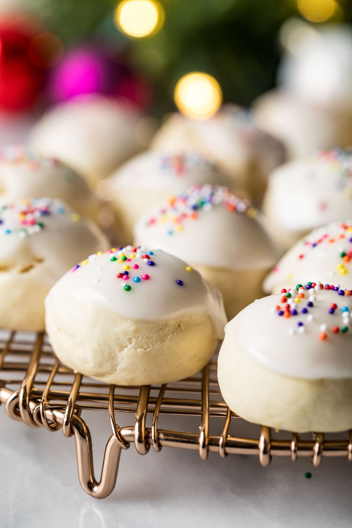Close-up view of pillowy, round cookies topped with a white icing and rainbow sprinkles.