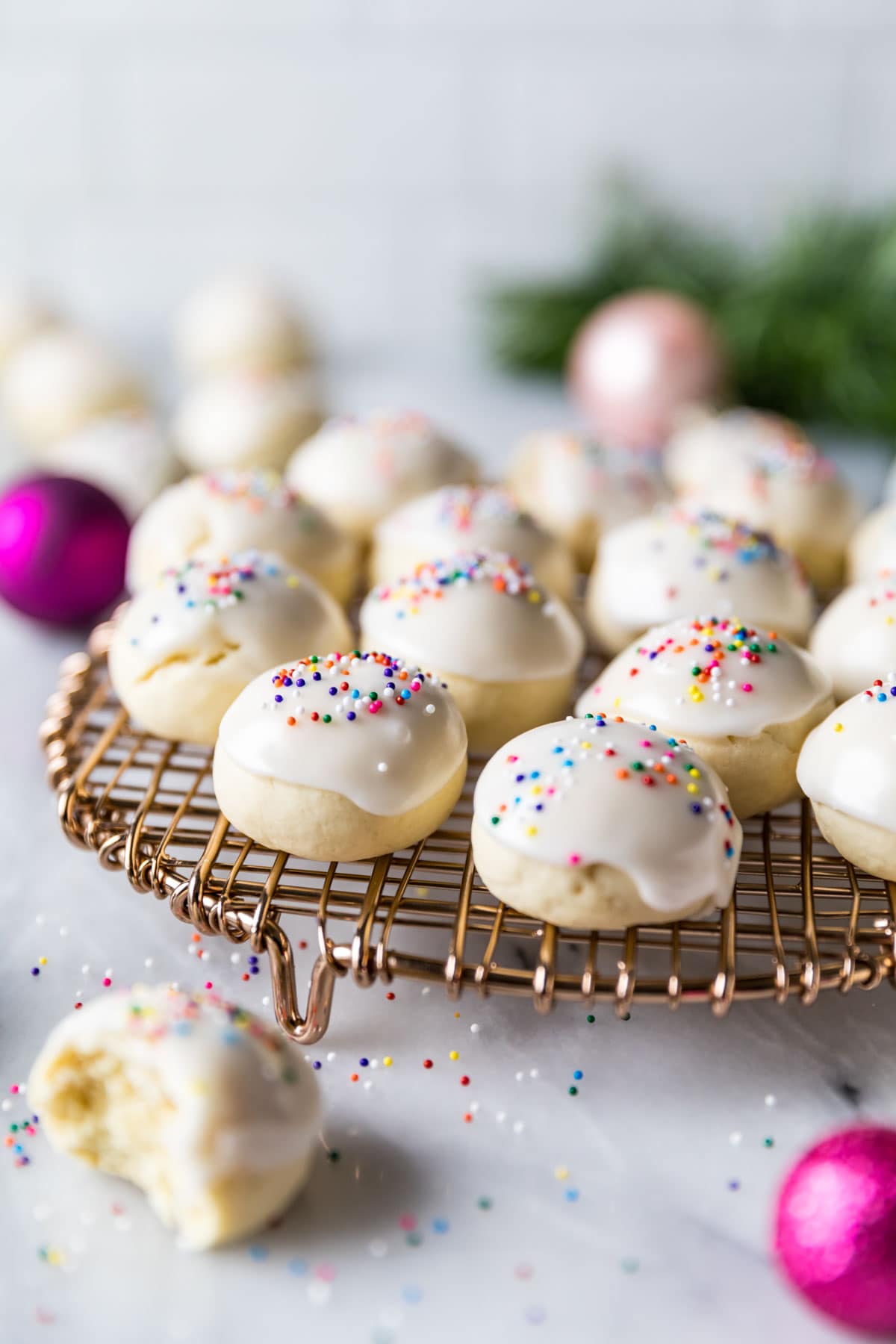 Close-up view of pillowy, round cookies topped with a white icing and rainbow sprinkles.