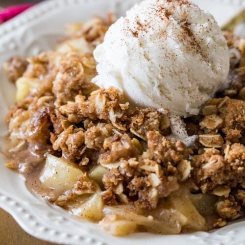 Bowl of apple crisp topped with a scoop of vanilla ice cream and cinnamon.