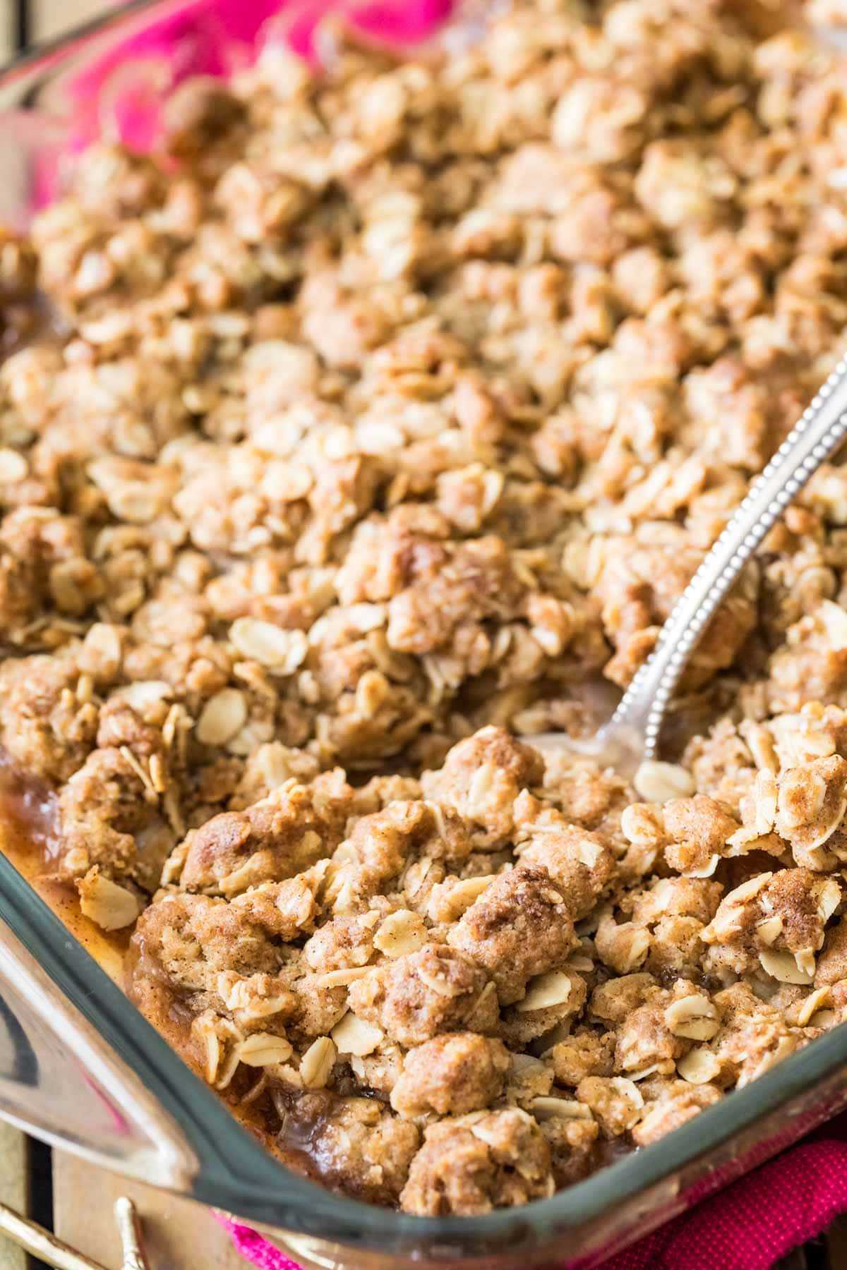 Spoon scooping a baked apple and oat crisp dessert out of a baking pan.