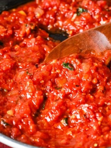 Pot of arrabiata sauce being stirred with a wood spoon.