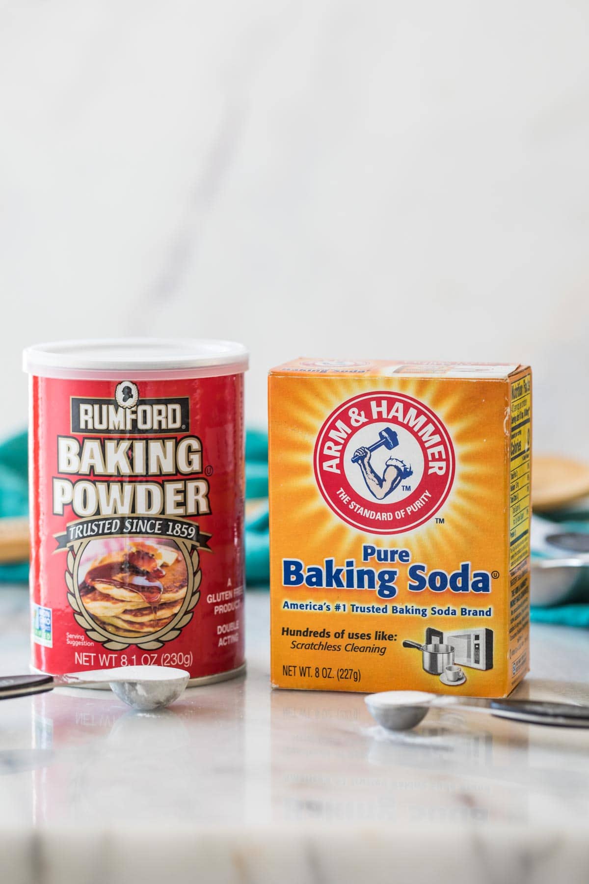 photo comparing baking powder vs. baking soda side by side with measuring spoons of each in front of their respective containers