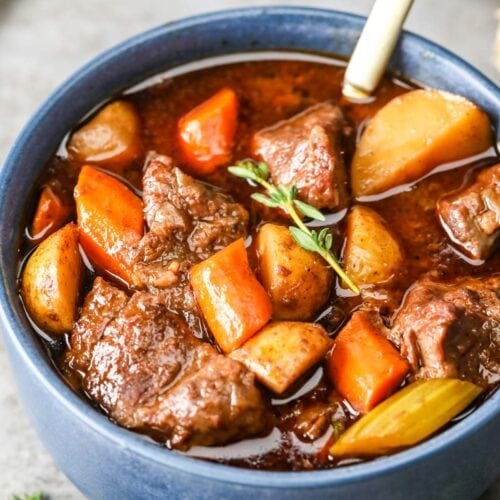 Blue bowl of beef stew with chunks of beef, carrots, and potatoes.