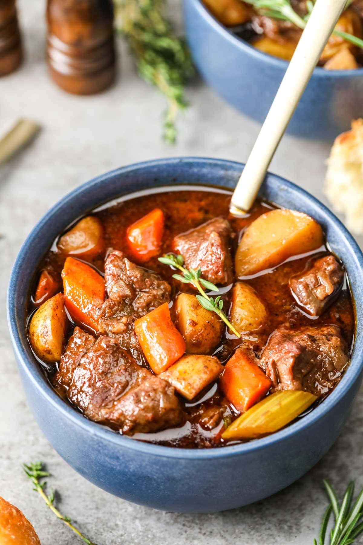 Blue bowl of beef stew with chunks of beef, carrots, and potatoes.