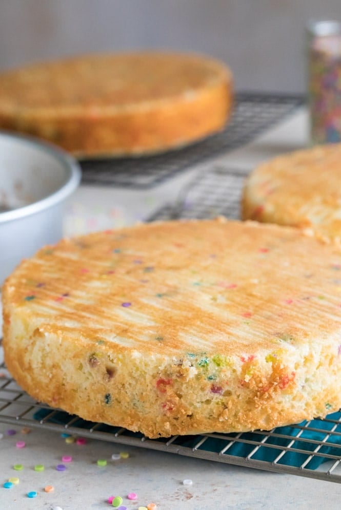 Three freshly baked layers of birthday cake cooling on wire rack