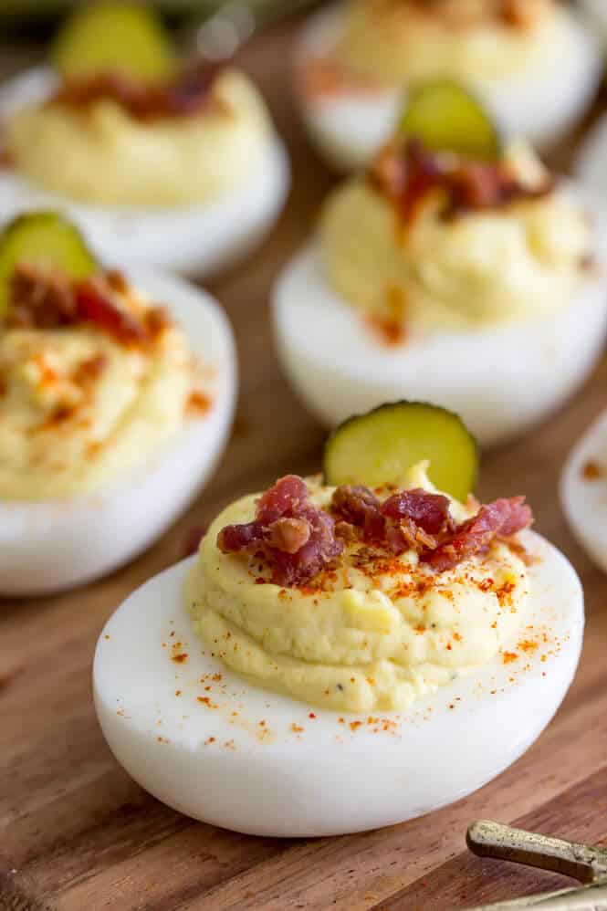 Deviled eggs topped off with paprika, bacon, and sweet pickle slices