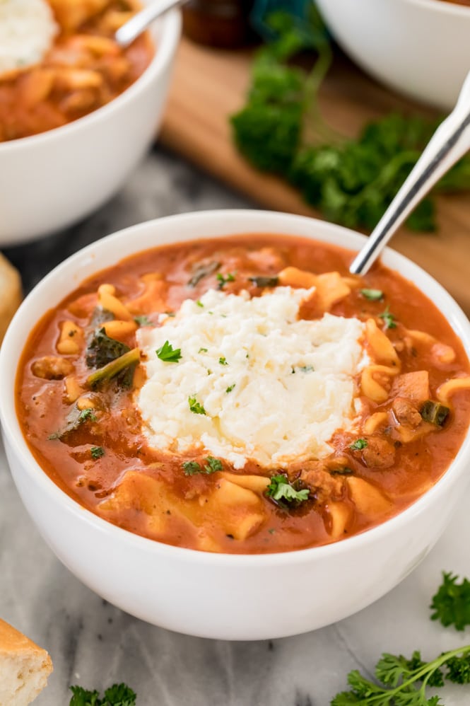 White bowl with lasagna soup topped with ricotta cheese