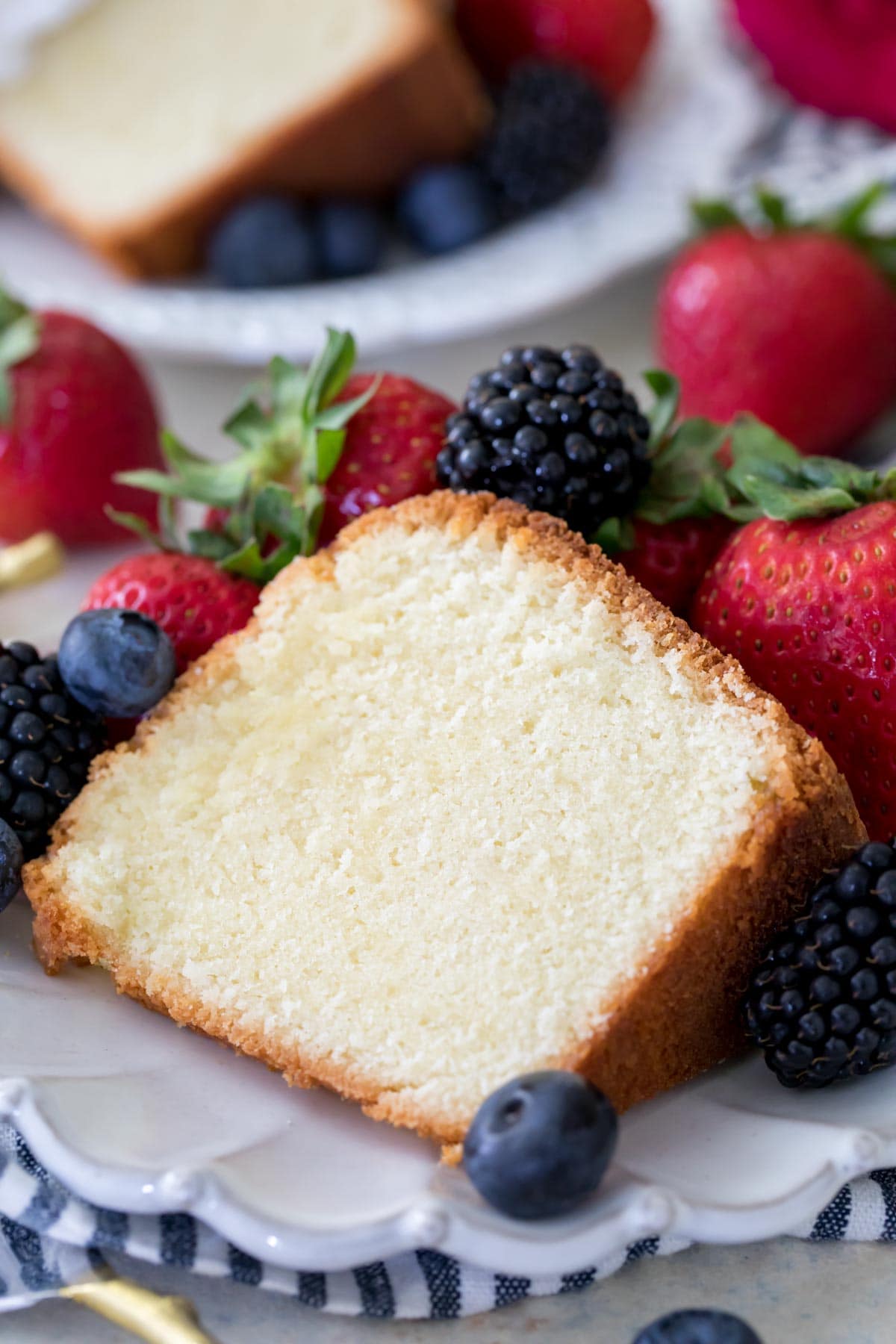 Thick slice of pound cake surrounded by fresh berries on white plate