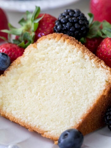 A slice of moist, buttery pound cake surrounded by fresh berries on a white plate