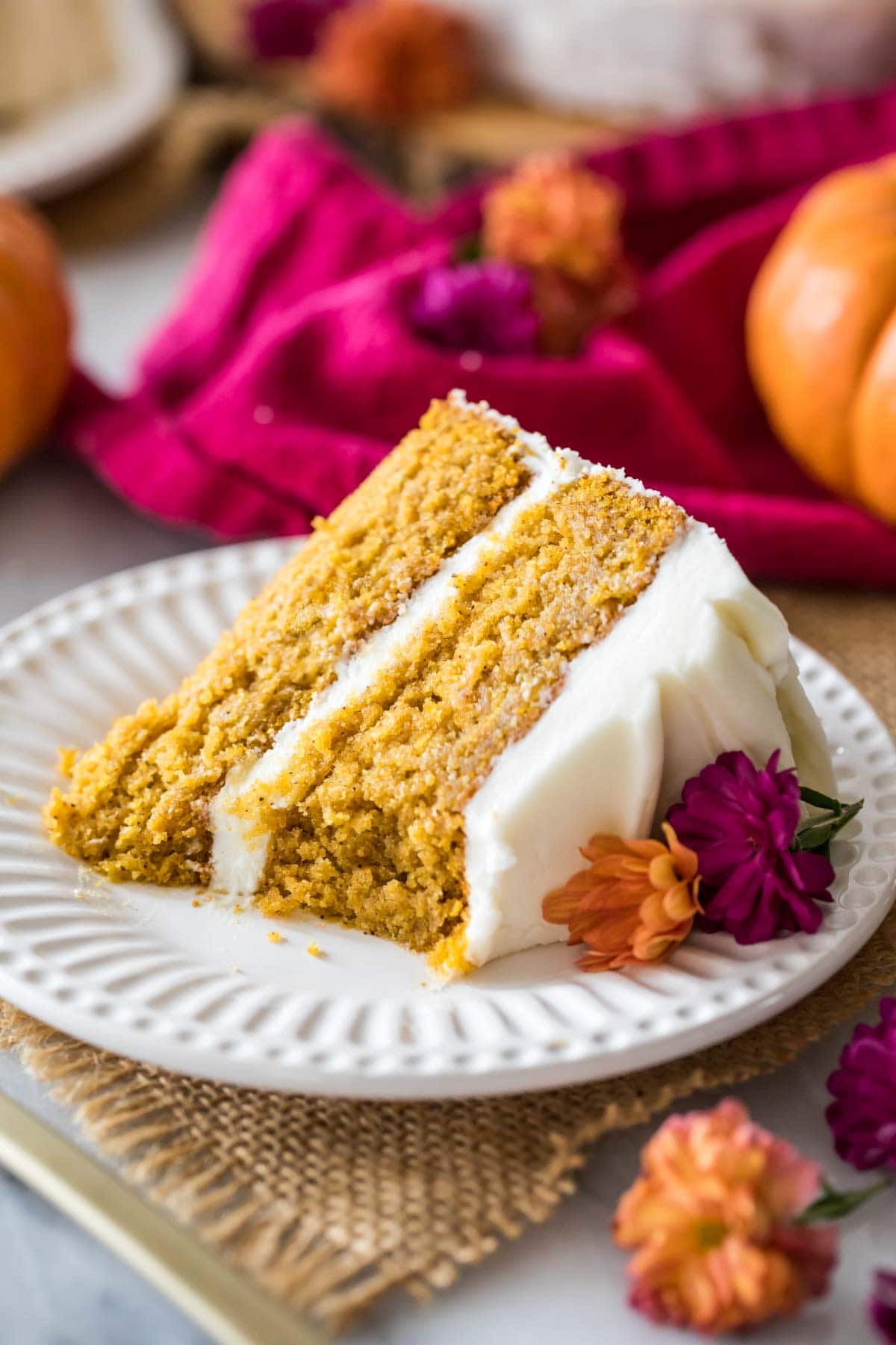 Slice of pumpkin cake frosted with cream cheese frosting on a white plate.