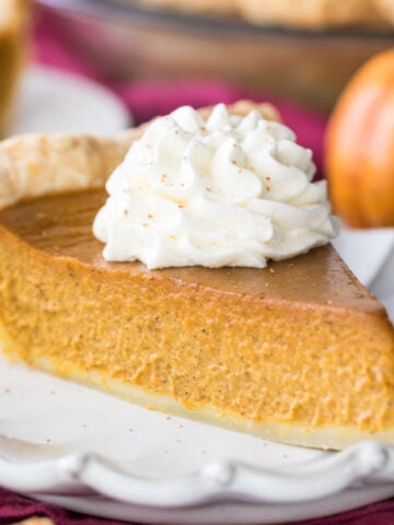 slice of homemade pumpkin pie topped with whipped cream on white plate