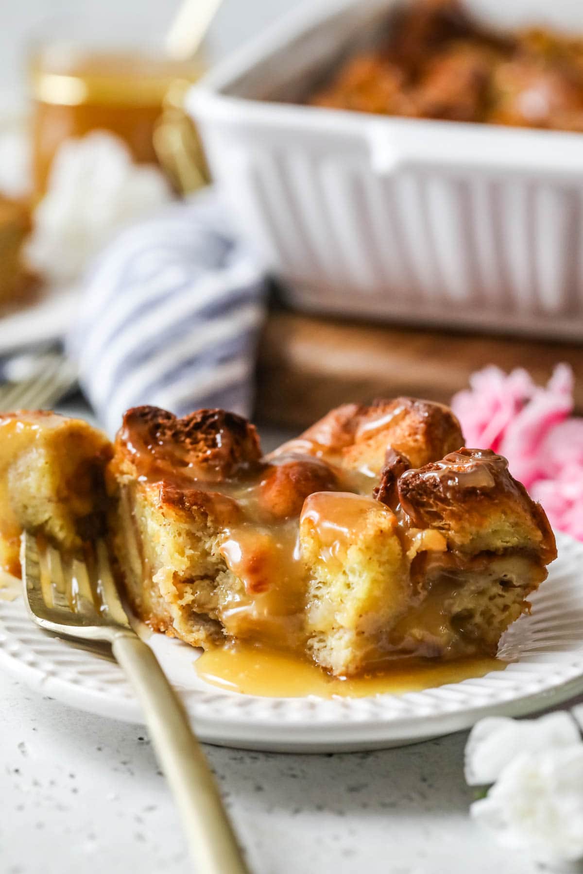 Slice of bread pudding drizzled with caramel sauce on a white plate.