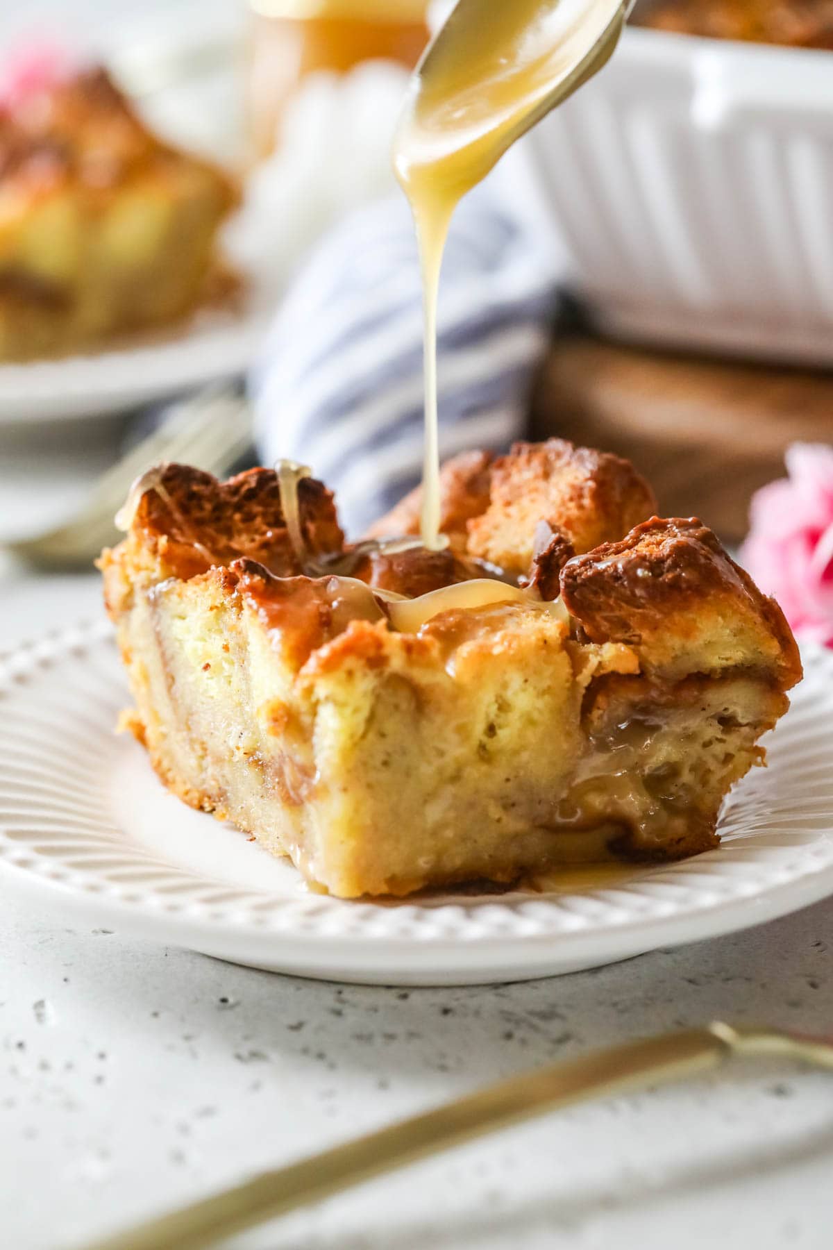 Sauce being poured over a square slice of a bread custard pudding.