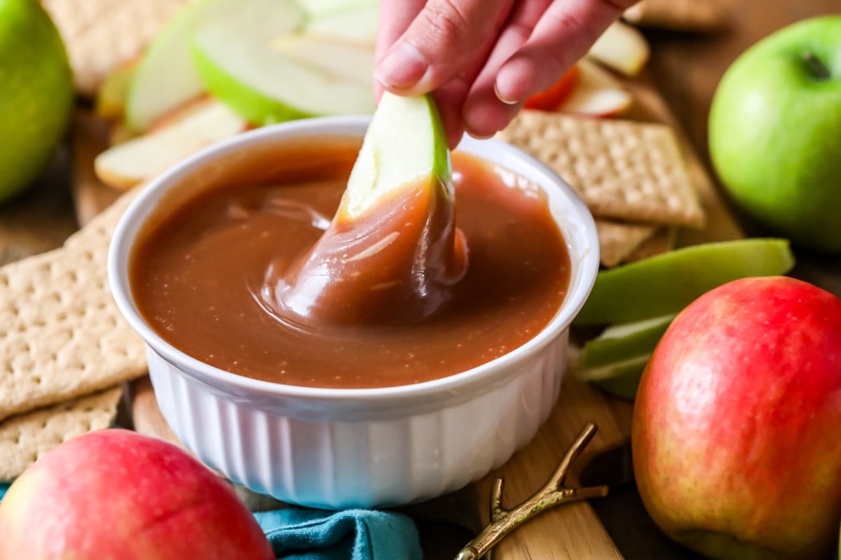 Apple slice being dunked into caramel dip.