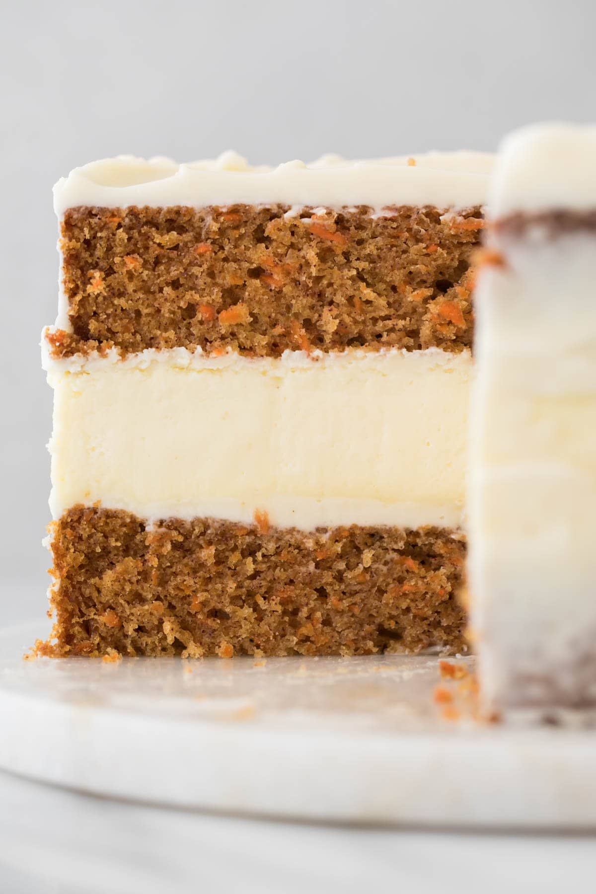 cross-section of a carrot cake cheesecake with a thick, smooth layer of cheesecake sandwiched between two layers of carrot cake