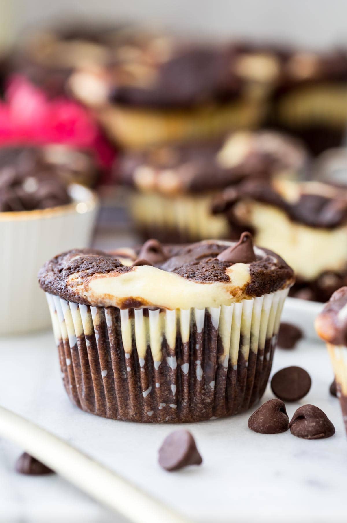 Chocolate and cheesecake swirled muffins on marble board. Pop of pink color from flower in background