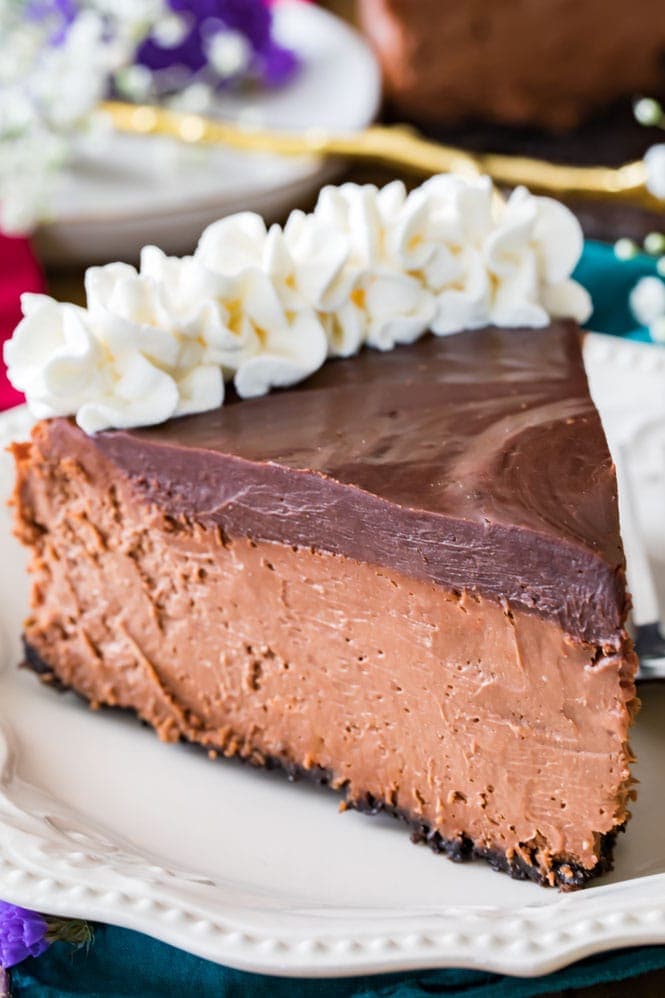A slice of chocolate cheesecake topped with chocolate ganache and whipped cream