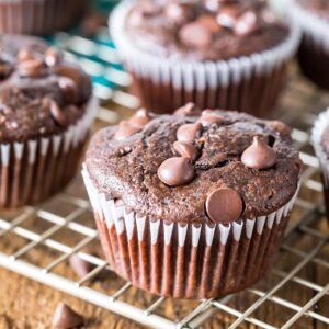 Chocolate zucchini muffins topped with chocolate chips on a metal cooling rack.