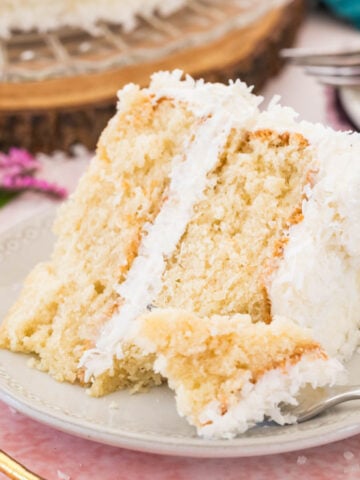 Slice of coconut cake on a plate with a forkful missing