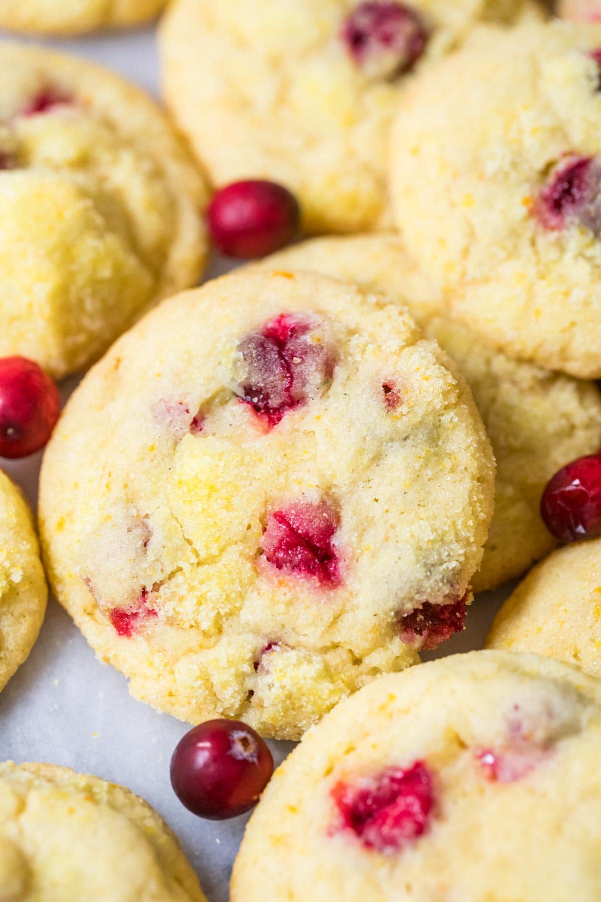 Orange cranberrry cookies in a pile surrounded by fresh cranberries.