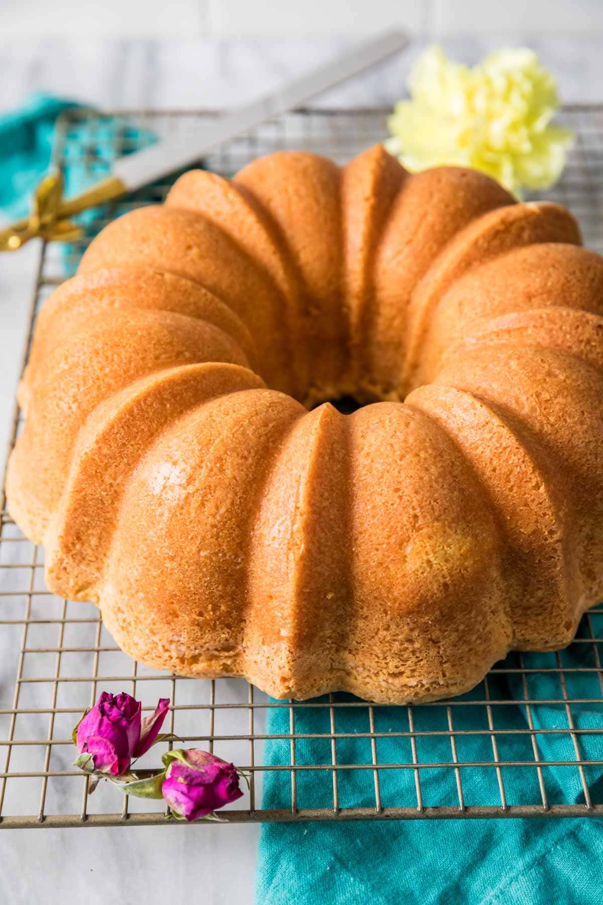 Whole pound cake that's been baked in a tube pan on a cooling rack with flowers.