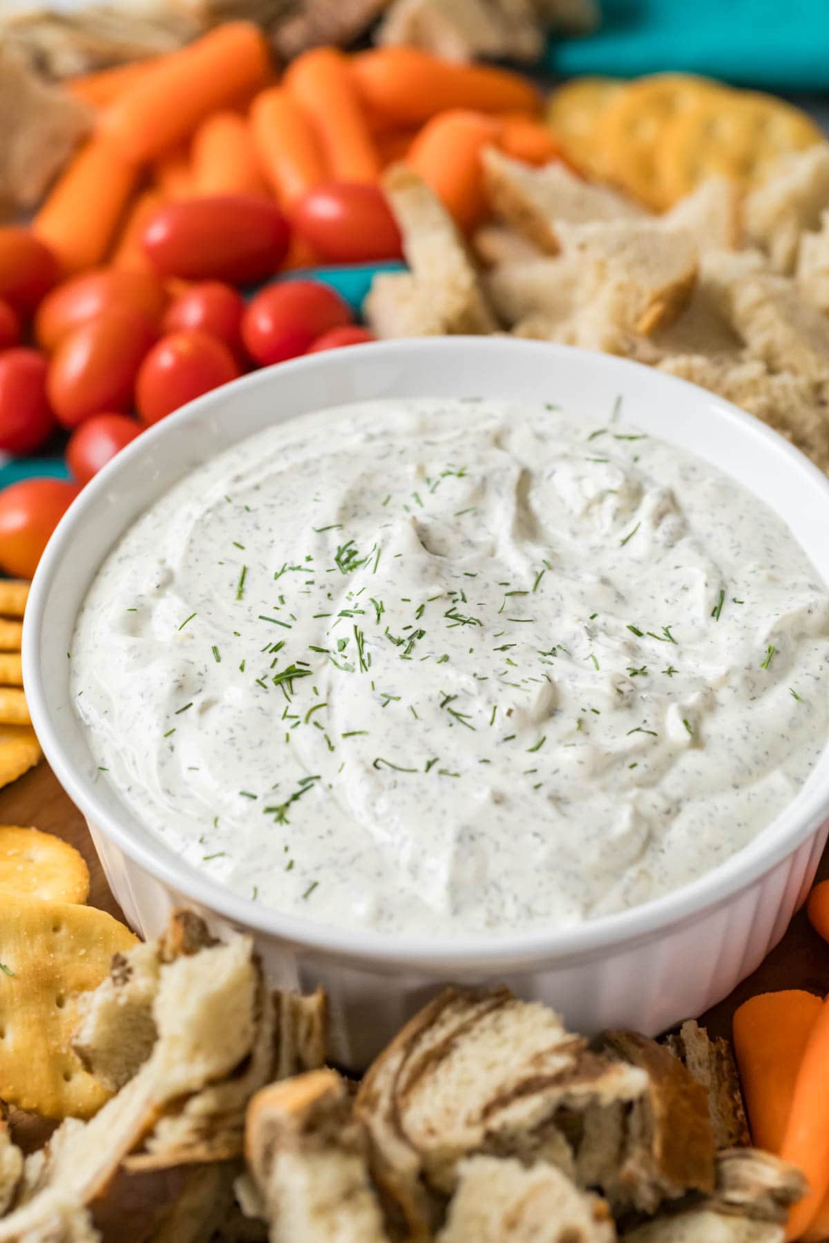 Bowl of dill dip with crackers, tomatoes, and bread surrounding it.