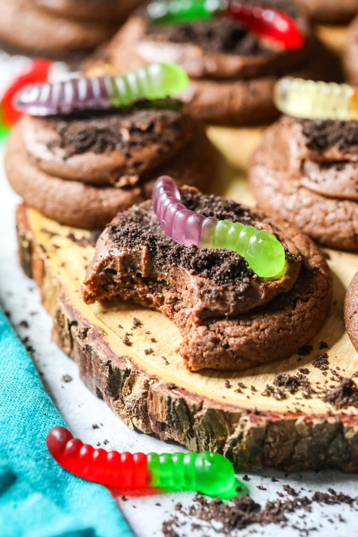 Bite missing from a chocolate cookie topped with Oreo crumbs and gummy worms.