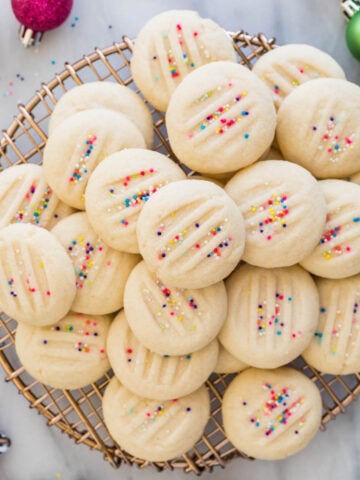 pile of whipped shortbread cookies with sprinkles on gold cooling rack
