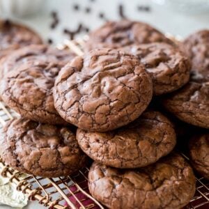 Crinkly-topped flourless chocolate cookies stacked in a pile on a metal cooling rack.