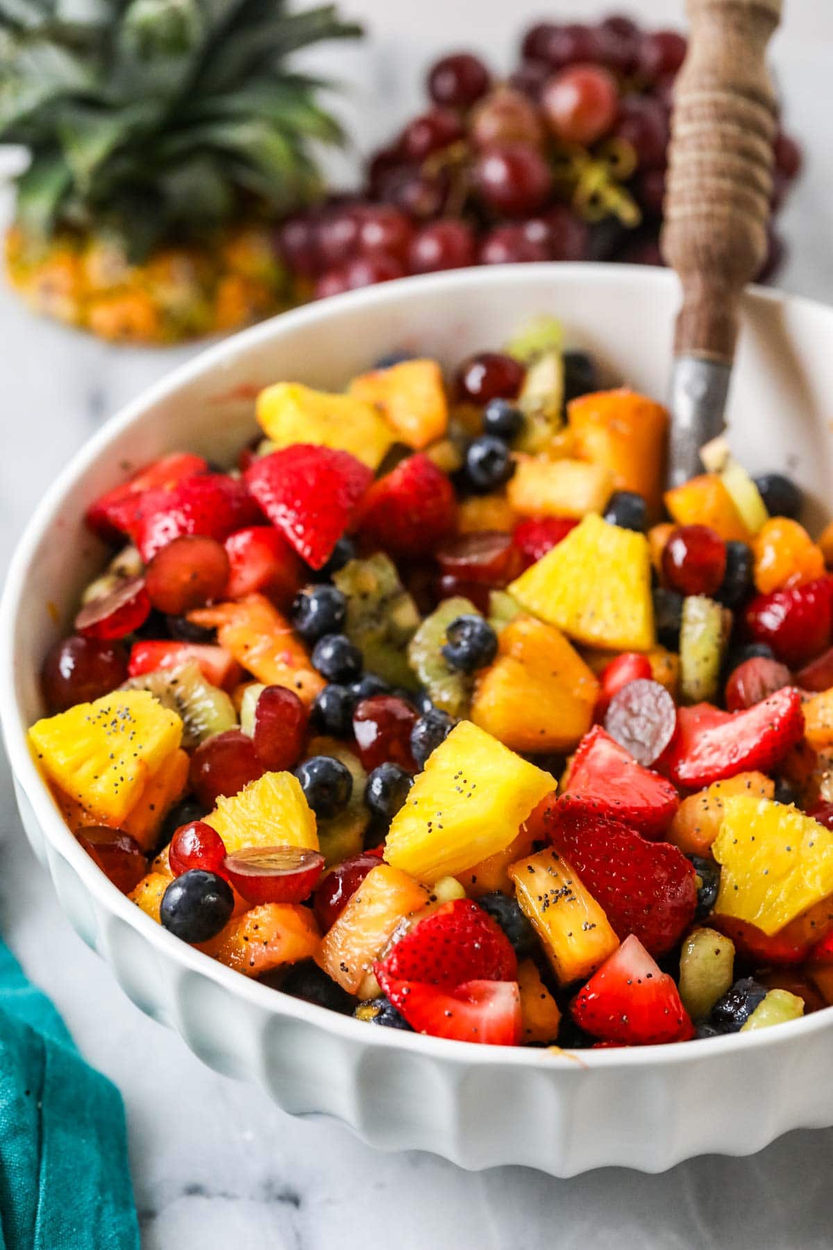 Large white serving bowl of a mixture of chopped berries, pineapple, oranges, and kiwis.