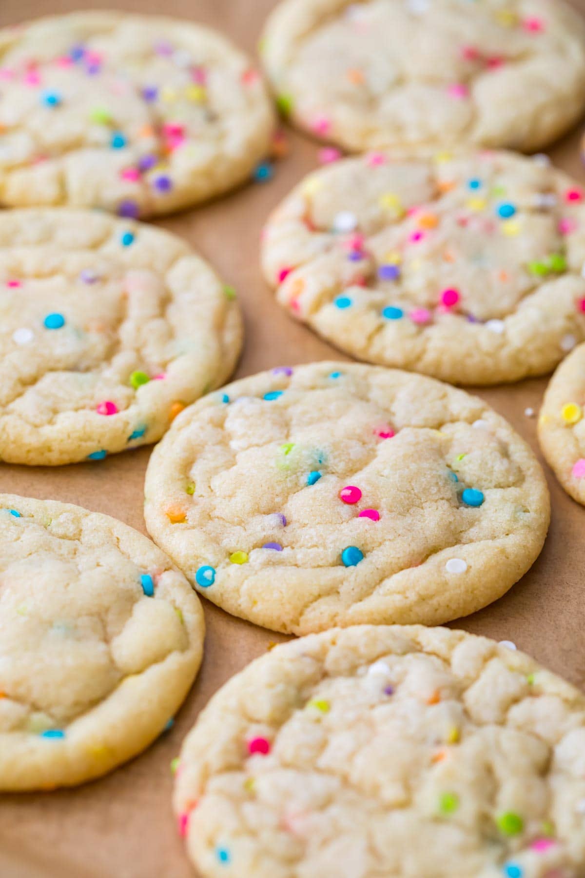 sugar cookies baked with colorful sprinkles resting on a parchment lined baking sheet