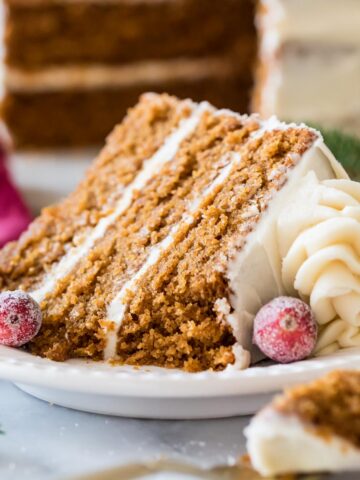 Slice of gingerbread layer cake topped with cream cheese frosting and sugared cranberries.