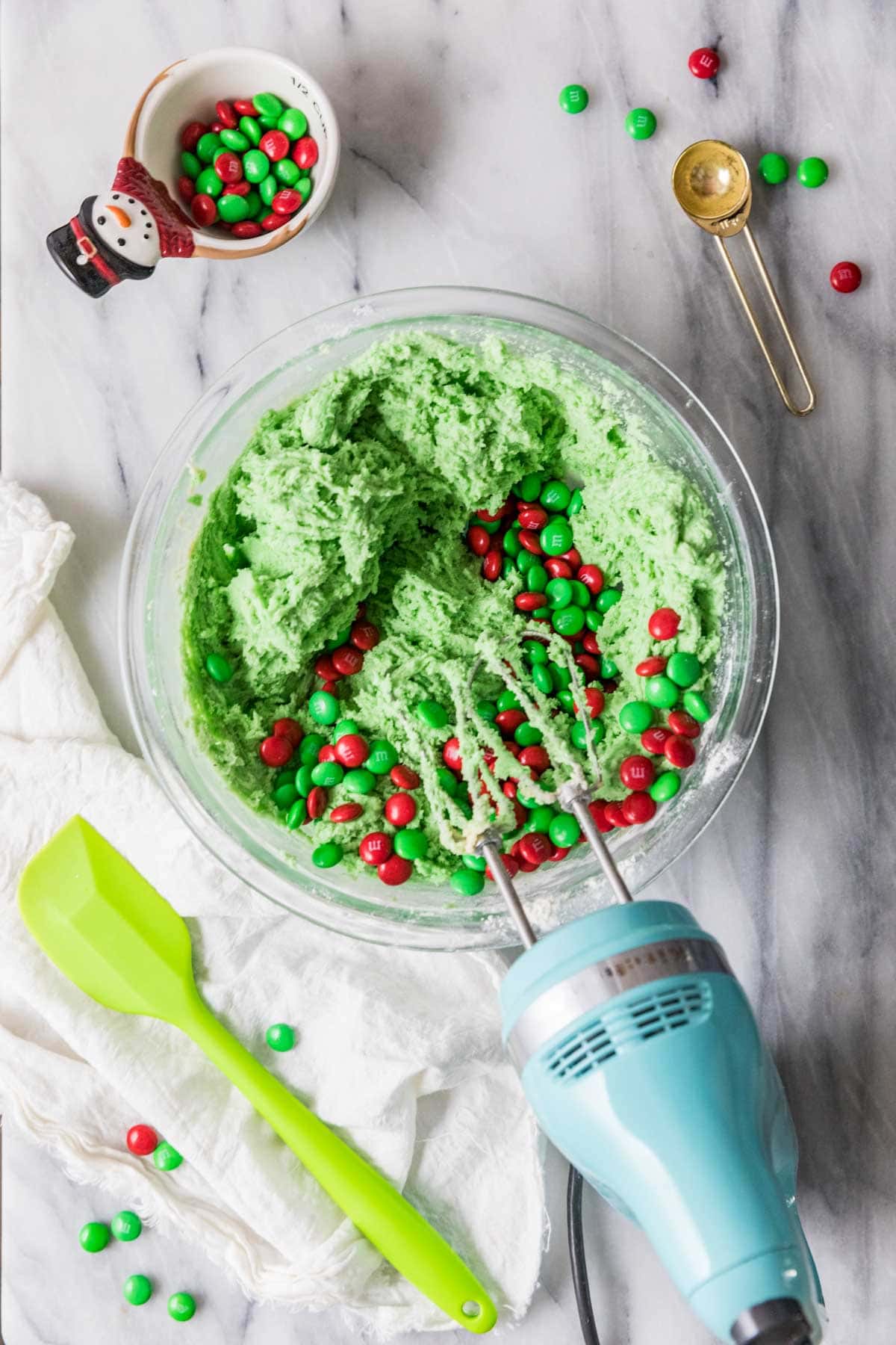 Overhead view of green cookie dough with red and green m&m candies about to be mixed in.