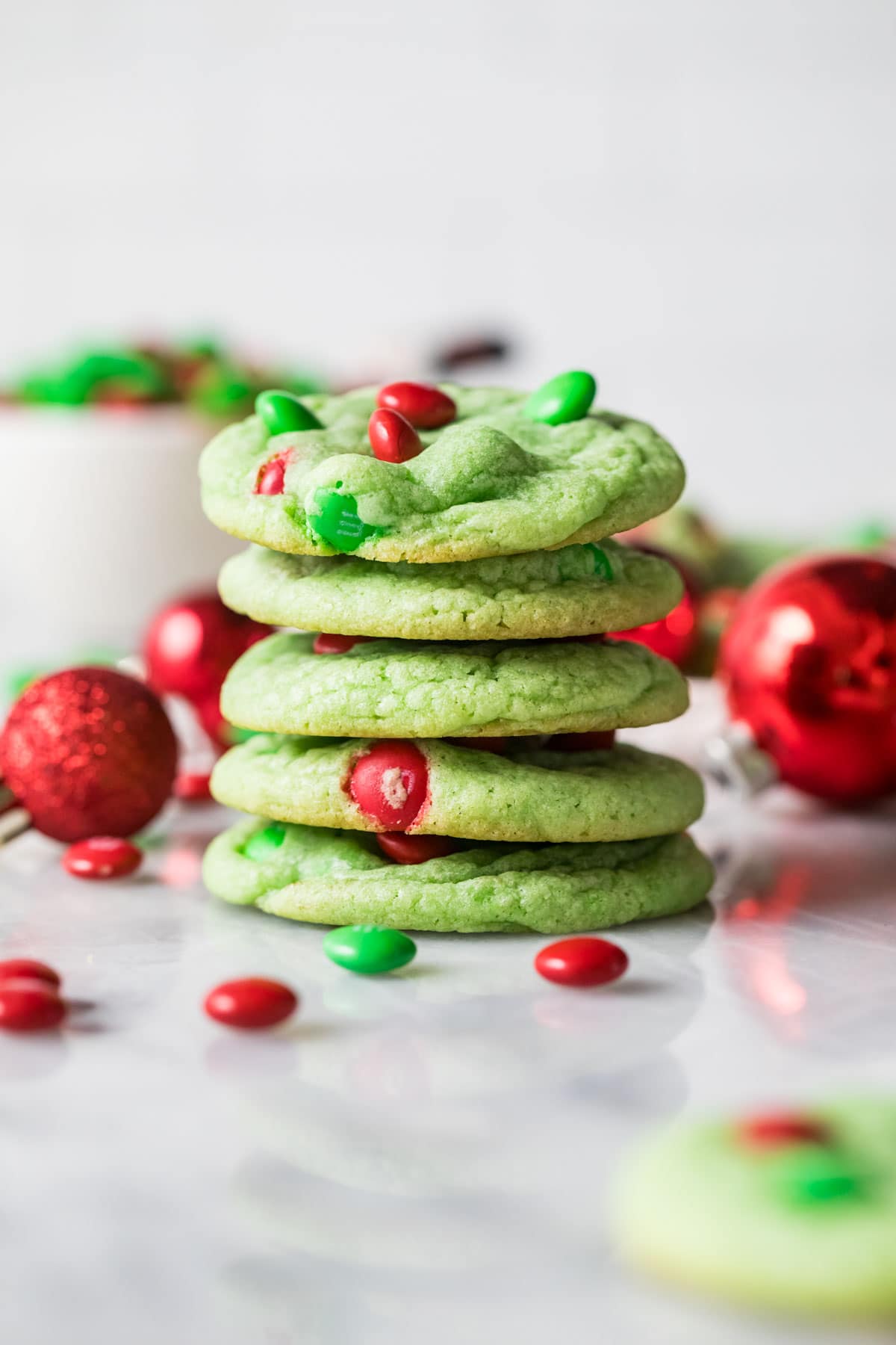 Stack of grinch cookies dyed a pale green color and decorated with red and green m&m candies.