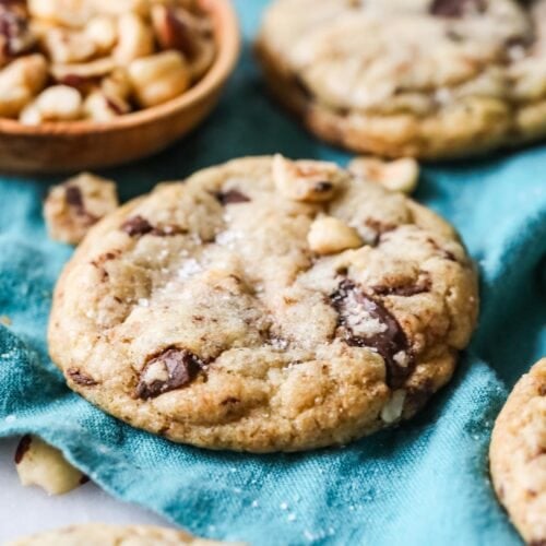 Hazelnut cookies with chocolate chips and sea salt resting on a teal tea towel.