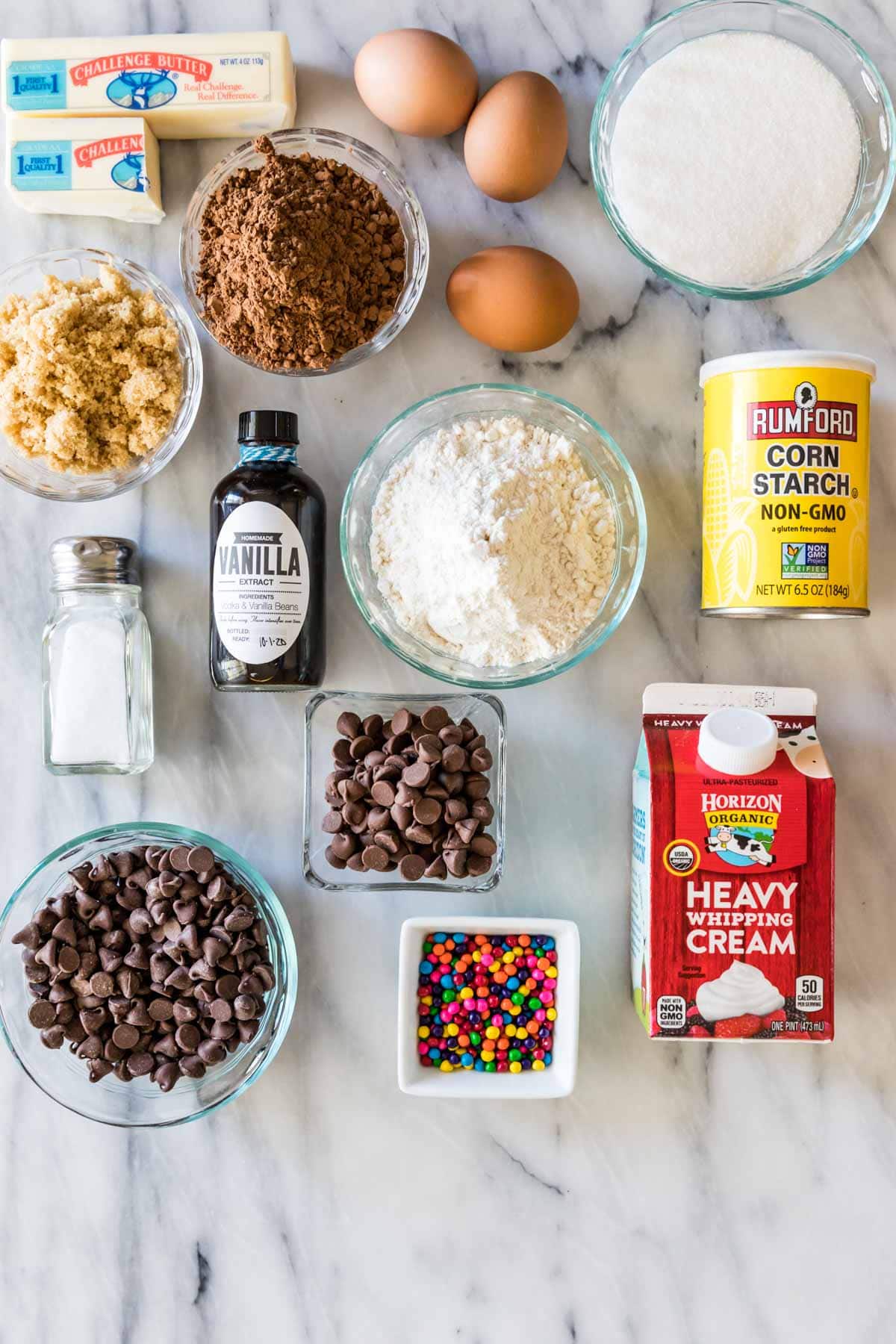 Overhead view of ingredients including chocolate chips, colorful candies, cocoa powder, heavy cream, and more.