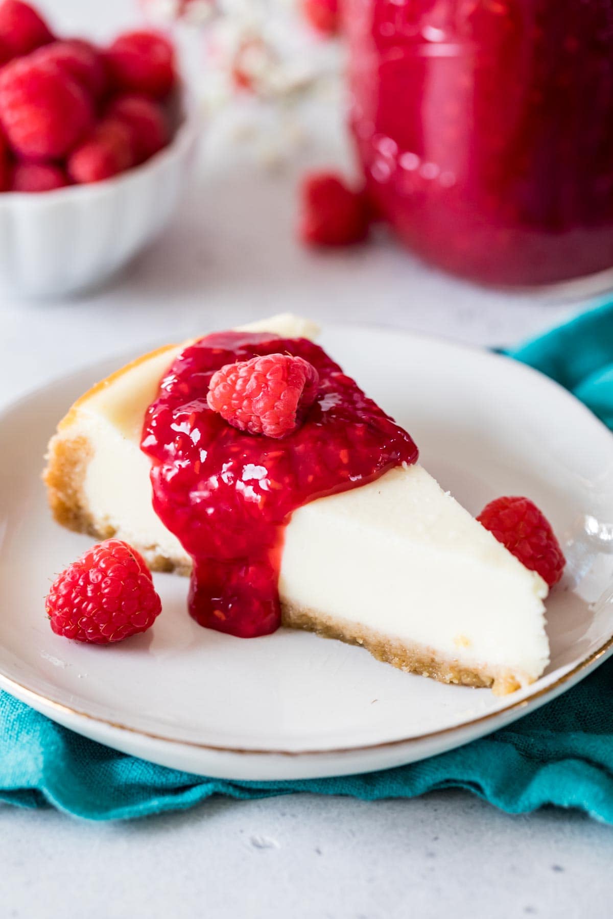 Slice of cheesecake topped with a red sauce and fresh raspberries.
