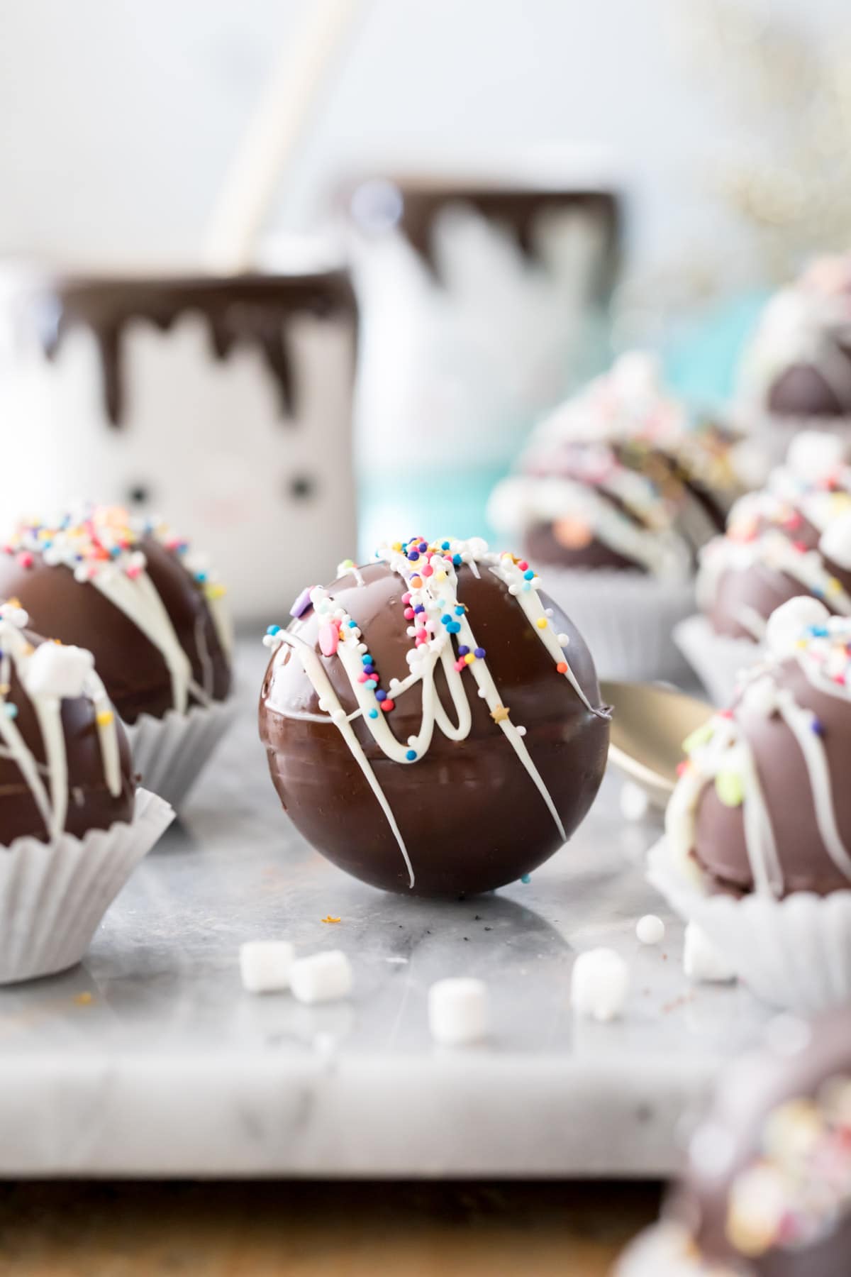 hot cocoa bombs on marble with mugs in background