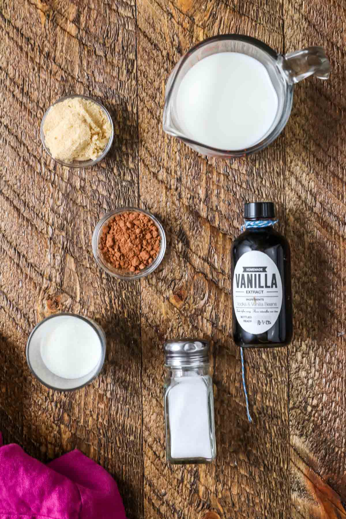 Overhead view of six ingredients including brown sugar, cocoa powder, salt, milk, cream, and vanilla.