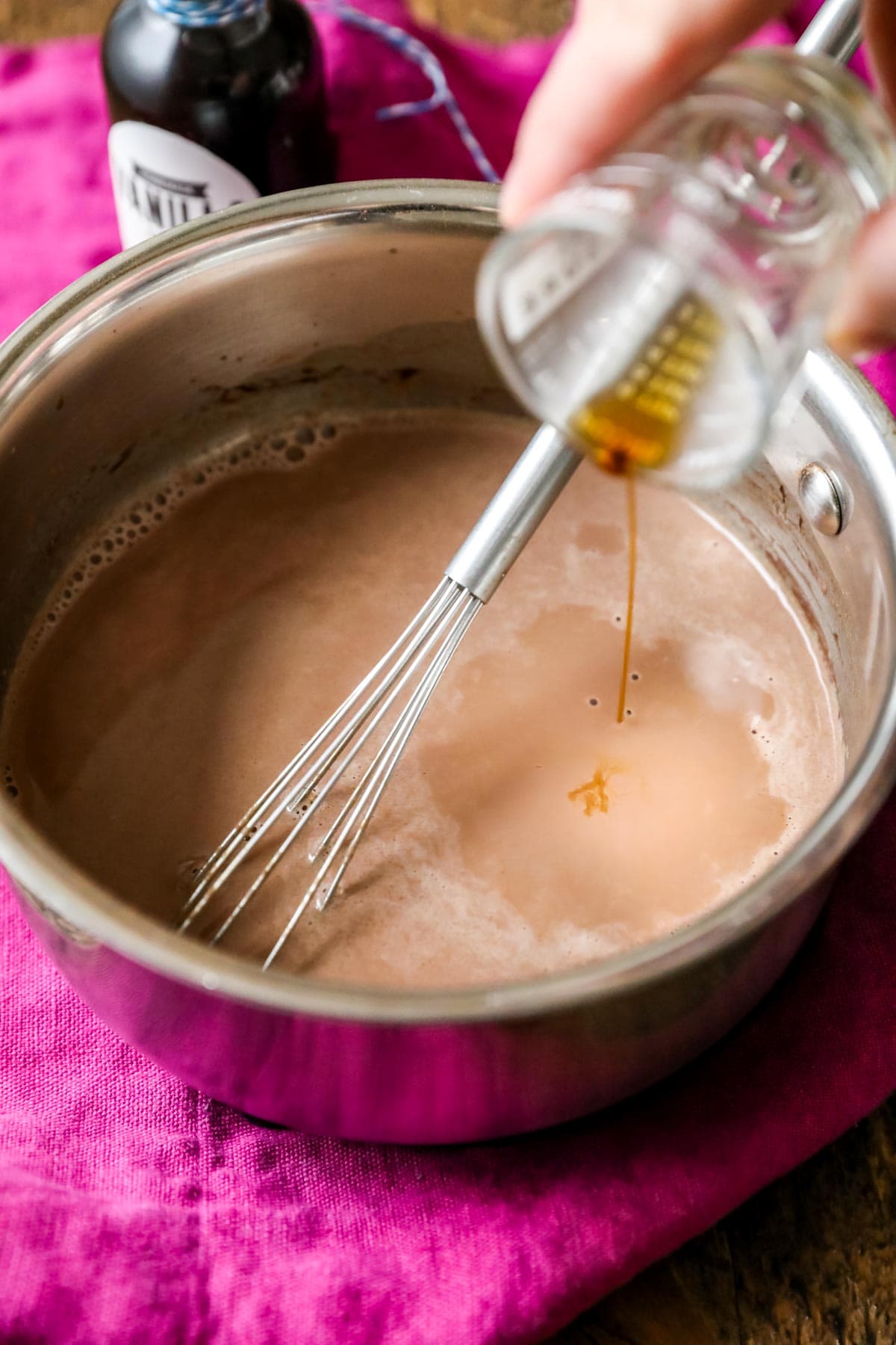 Vanilla extract being poured into a milk, cream, and cocoa mixture on the stove.