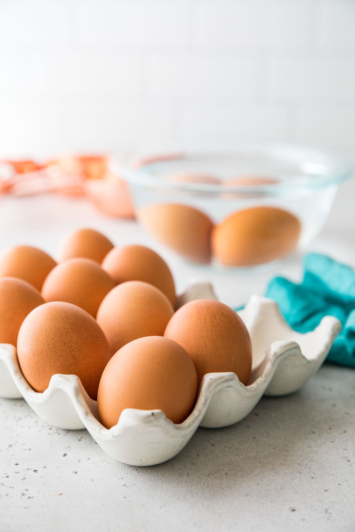 brown eggs in an egg carton with two eggs in a bowl of water in the background