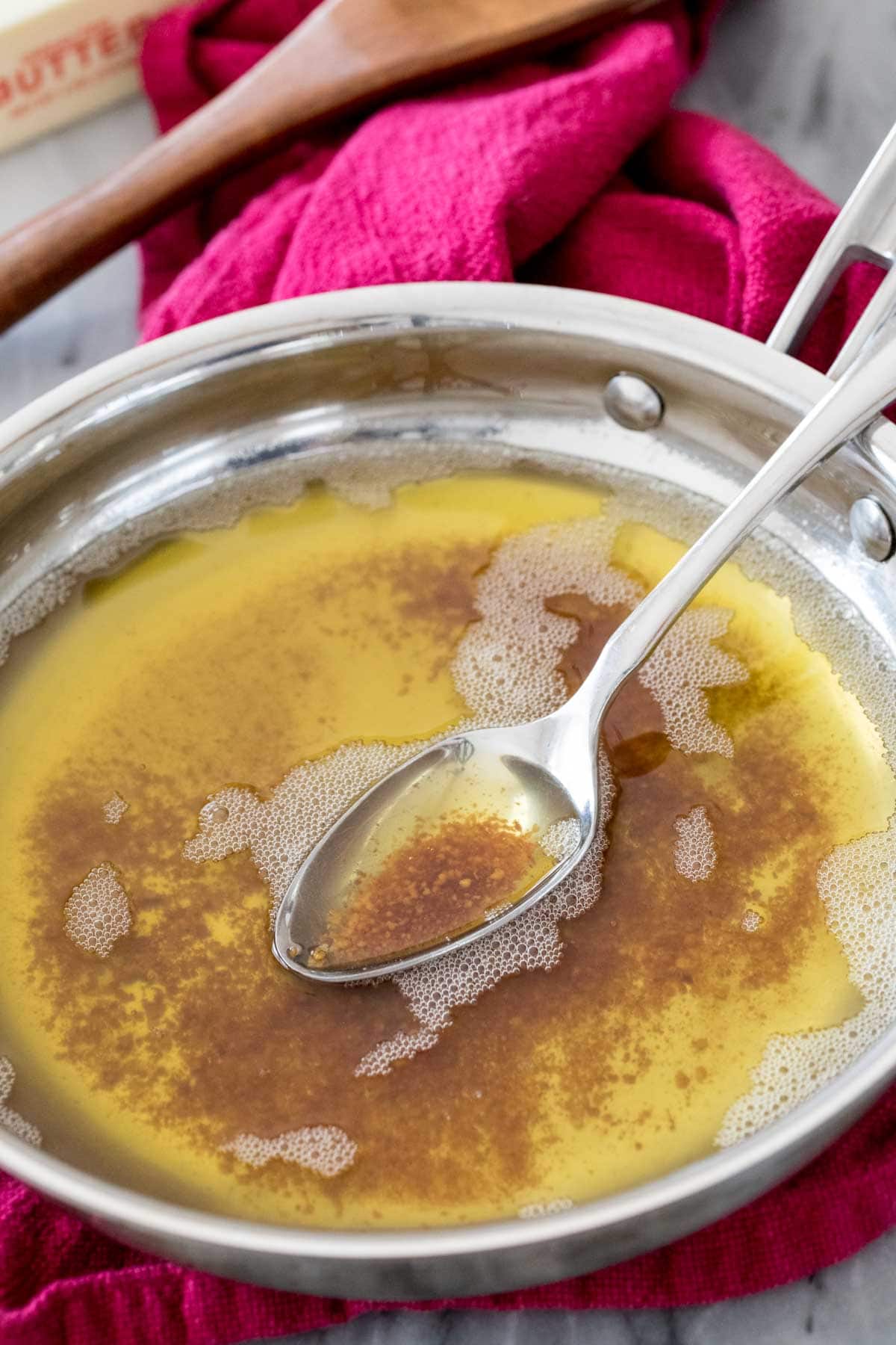 metal spoon scooping out golden brown melted butter from a stainless steel pan
