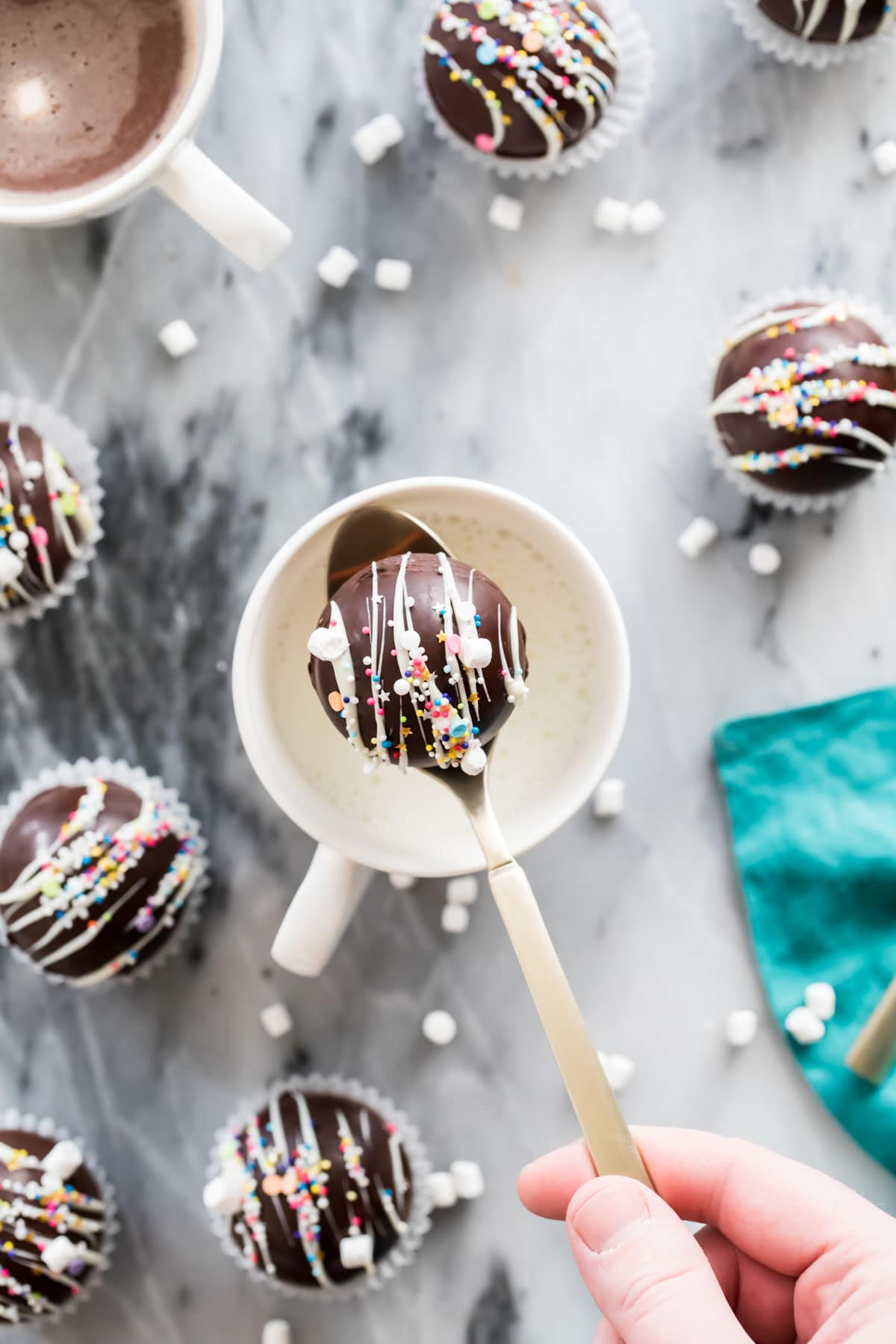 hot chocolate bomb on gold spoon over mug of milk