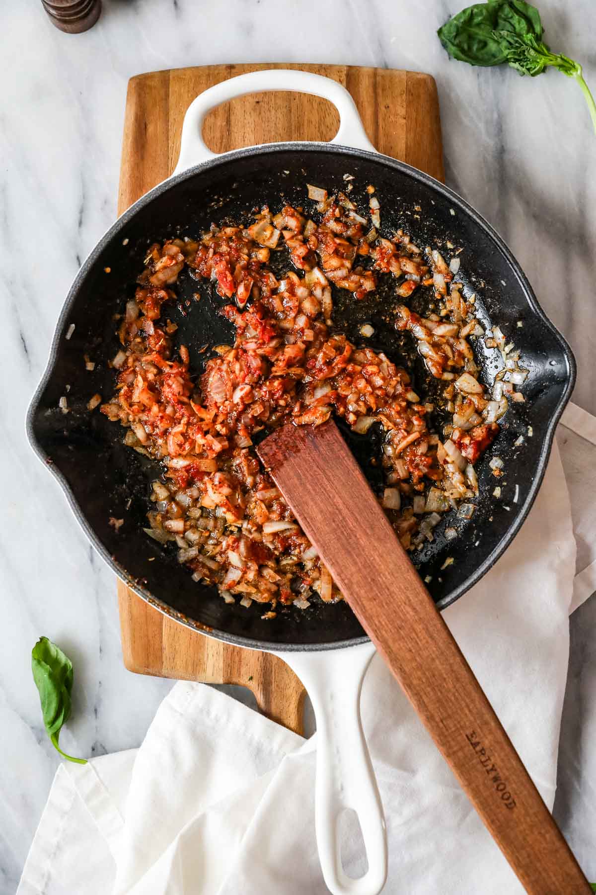 Overhead view of tomato paste being stirred into a pan of onion and garlic.