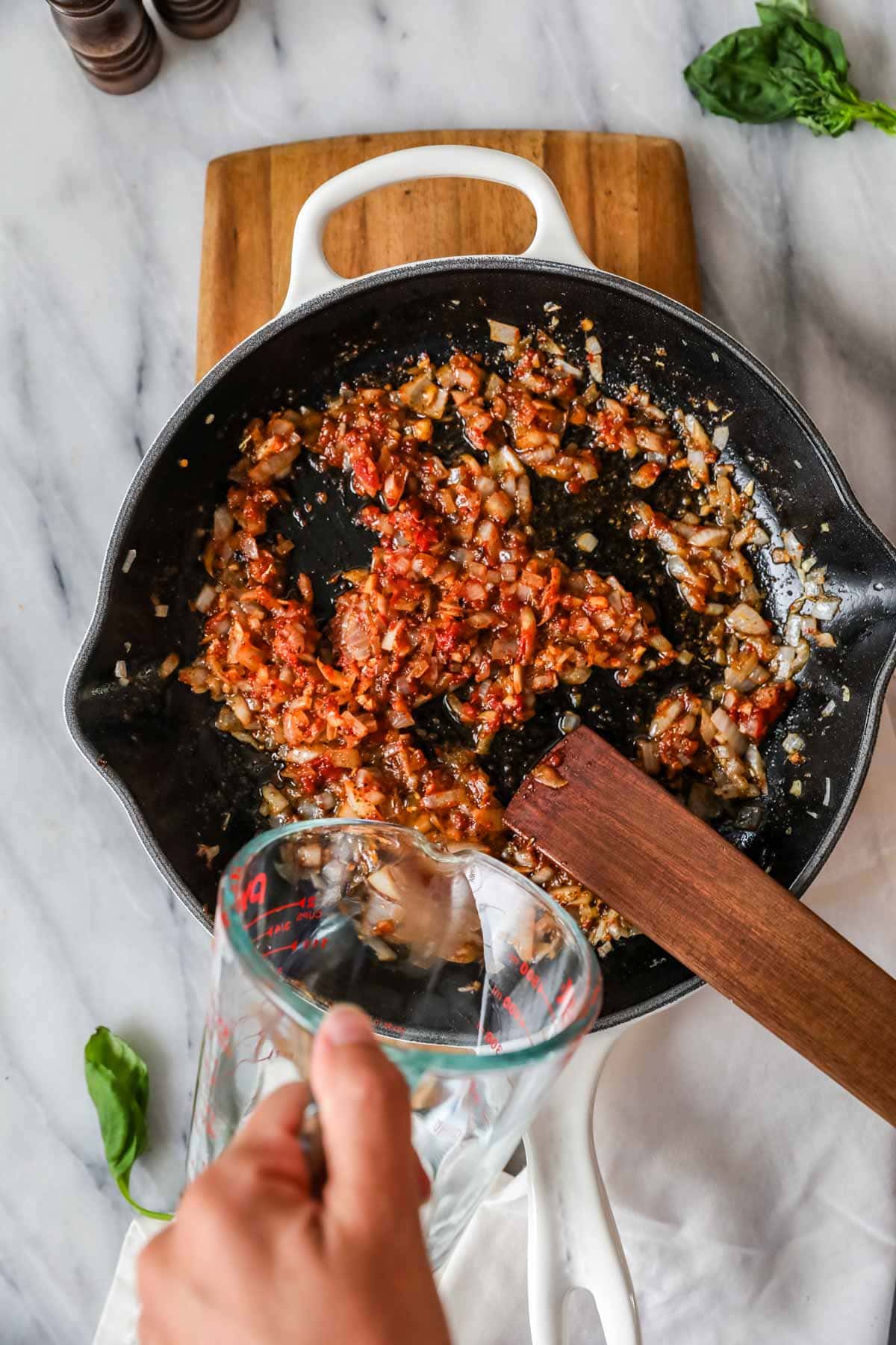 Overhead view of vodka being poured into a pan of onions, garlic, and tomato paste.