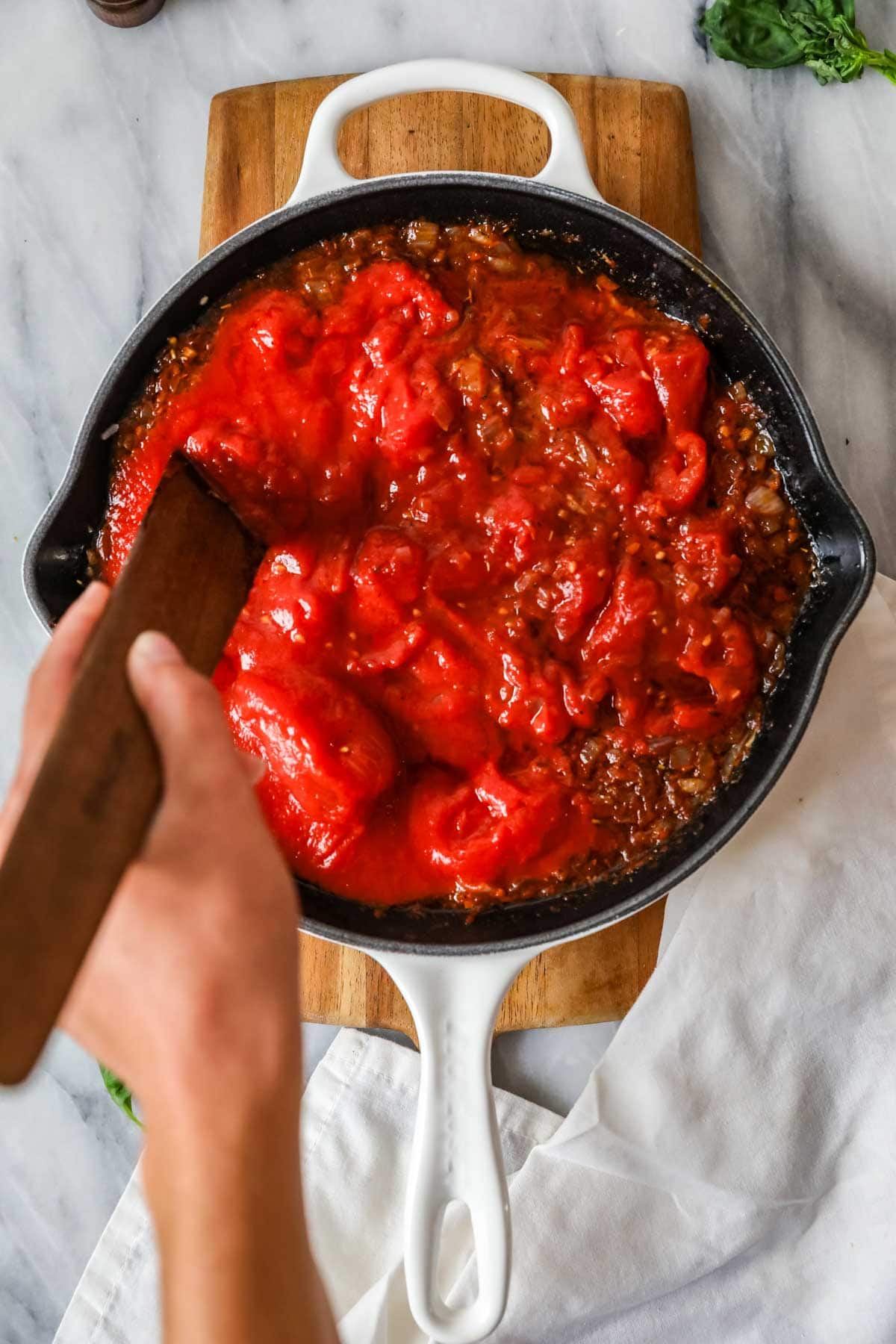 Overhead view of canned tomatoes being stirred into cast iron skillet.