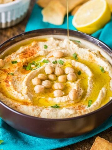 Large bowl of homemade hummus topped with paprika, parsley, olive oil, and chickpeas.