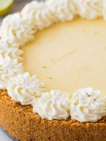 close-up view of a whole key lime cheesecake topped with a decorative whipped cream border and lime zest