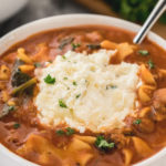 Lasagna soup topped with ricotta cheese mixture in white bowl